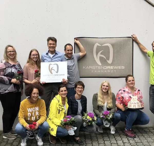 Das Team feiert vor dem Praxisschild